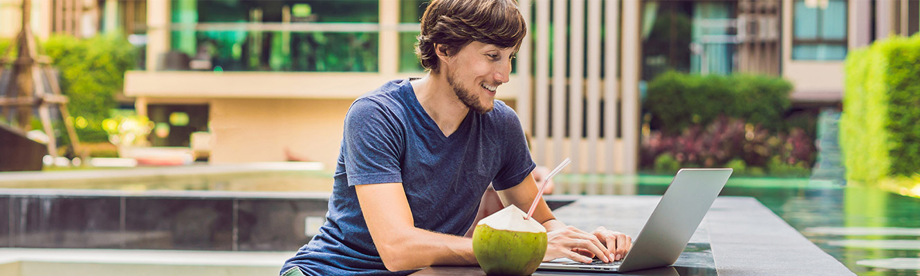 Young man on vacation sitting outside with laptop.