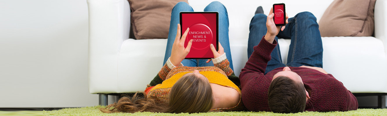 Young couple lying in the floor looking at Enrichment News page on their smart devices. 