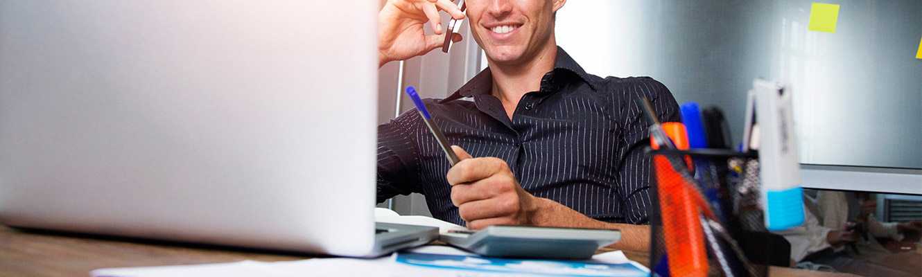 Young man talking on phone sitting at laptop.