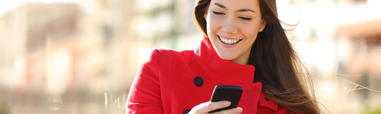 Young woman in red jacket holding phone with city background. 